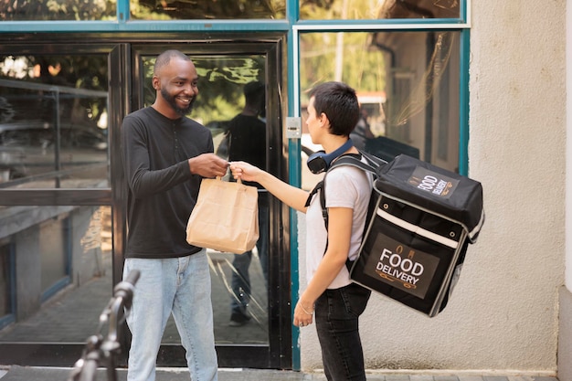 food delivery service young woman courier giving client lunch paper bag smiling african american customer taking restaurant takeaway meal outdoors woman holding package medium shot 482257 53127 1